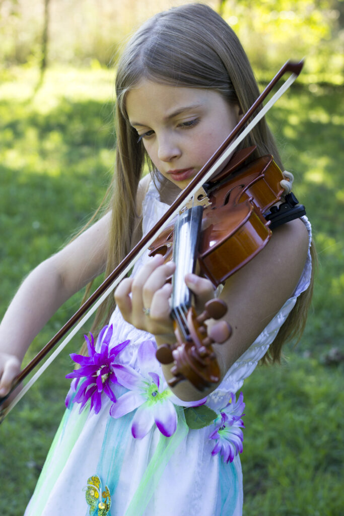 Cute little girl in white dress with flowers playing violine in the public park