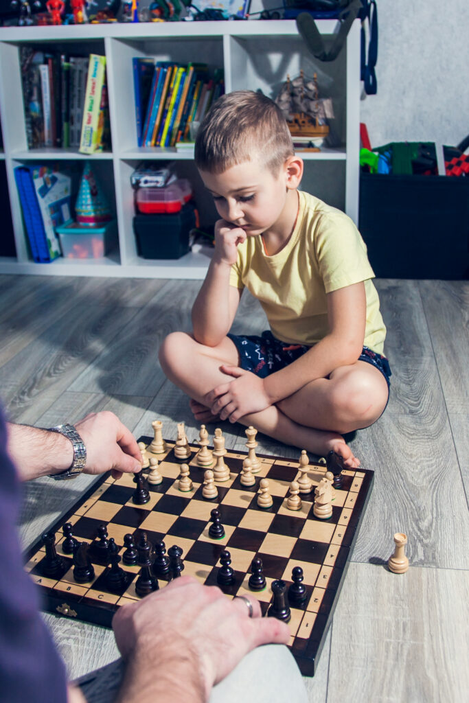 Dad and son play chess on the floor in the children's room among the toys.